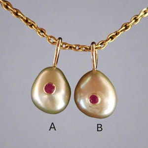 Op de afbeelding: Twee gouden hangers, elk met een enkele robijn edelsteen, hangen aan een gouden ketting. De hangers zijn traanvormig en zijn gemarkeerd met A en B.