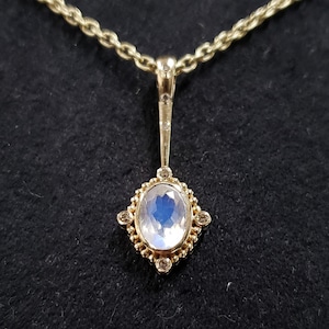 Op de afbeelding: Een gouden ketting met een hanger met een grote ovale maansteen omringd door kleinere diamanten in een gouden zetting.