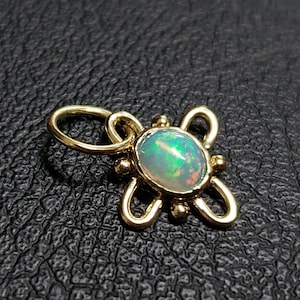 May include: A gold pendant with a delicate, ornate design featuring a round opal gemstone. The opal has a milky white base with flashes of green and orange.