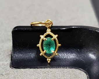 May include: A gold pendant with a green emerald gemstone set in a detailed, ornate design.