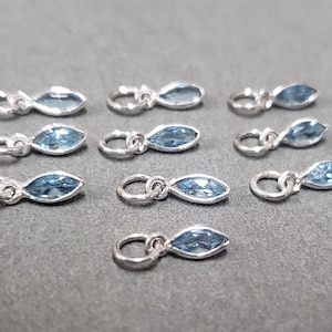 Op de afbeelding: Tien zilveren bedels met lichtblauwe marquise-vormige edelstenen. Elke bedel heeft een kleine lus om aan een armband of ketting te bevestigen.