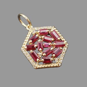 May include: A gold pendant in a hexagonal shape featuring a cluster of baguette-cut red rubies arranged in a geometric pattern. The outer border of the hexagon is lined with small, round, clear white diamonds set in a gold frame with a bail.