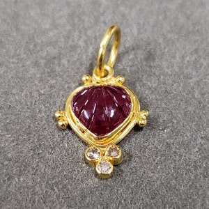 May include: A gold pendant featuring a carved ruby heart with three small diamonds hanging from the bottom.