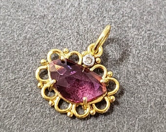 May include: A gold pendant with a teardrop-shaped, faceted purple gemstone. The pendant is accented with a small diamond and a decorative gold filigree border. The bail is also gold.