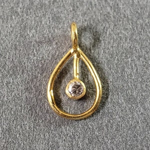 Può includere: Un ciondolo a forma di lacrima in oro con una piccola pietra preziosa trasparente appesa all'interno.