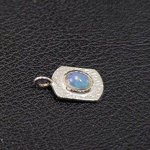 May include: A silver pendant with a textured surface and a round opal gemstone in the center.