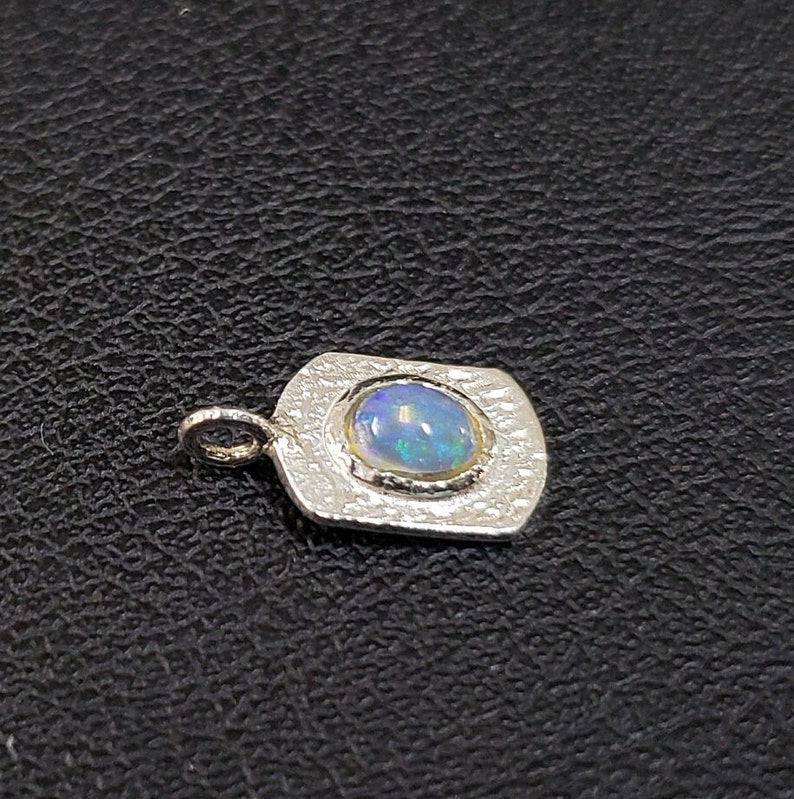 May include: A silver pendant with a textured surface and a round opal gemstone in the center.