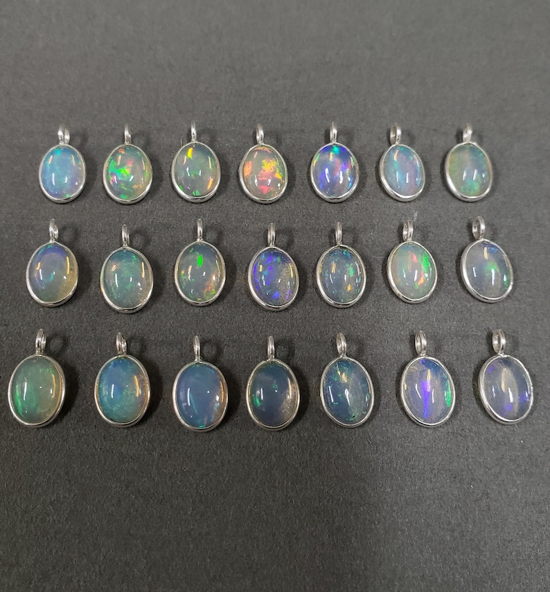 May include: Twenty oval-shaped opal pendants with silver settings. The opals are iridescent with shades of blue, green, and purple.