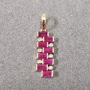 May include: A gold pendant with a vertical design featuring multiple rectangular ruby gemstones and smaller round diamonds.
