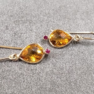 May include: A pair of gold dangle earrings with teardrop-shaped topaz gemstones and small ruby accents.