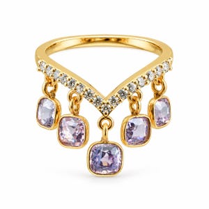 Puede incluir: Un anillo dorado en forma de V con una banda engastada con pequeñas piedras redondas transparentes. Cinco piedras preciosas de color violeta claro y corte cuadrado cuelgan de la banda, cada una sujeta por una pequeña anilla dorada.