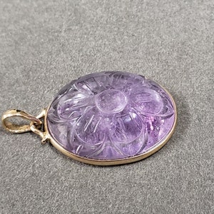 Op de afbeelding: Een hanger van paarse amethyst met een gegraveerd bloemmotief, gezet in goud.