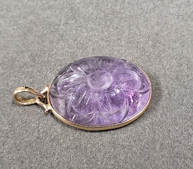 Op de afbeelding: Een hanger van paarse amethyst met een gegraveerd bloemmotief, gezet in goud.