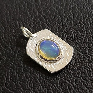 May include: A silver pendant with a textured rectangular design featuring a round opal gemstone with blue and green iridescent colors.