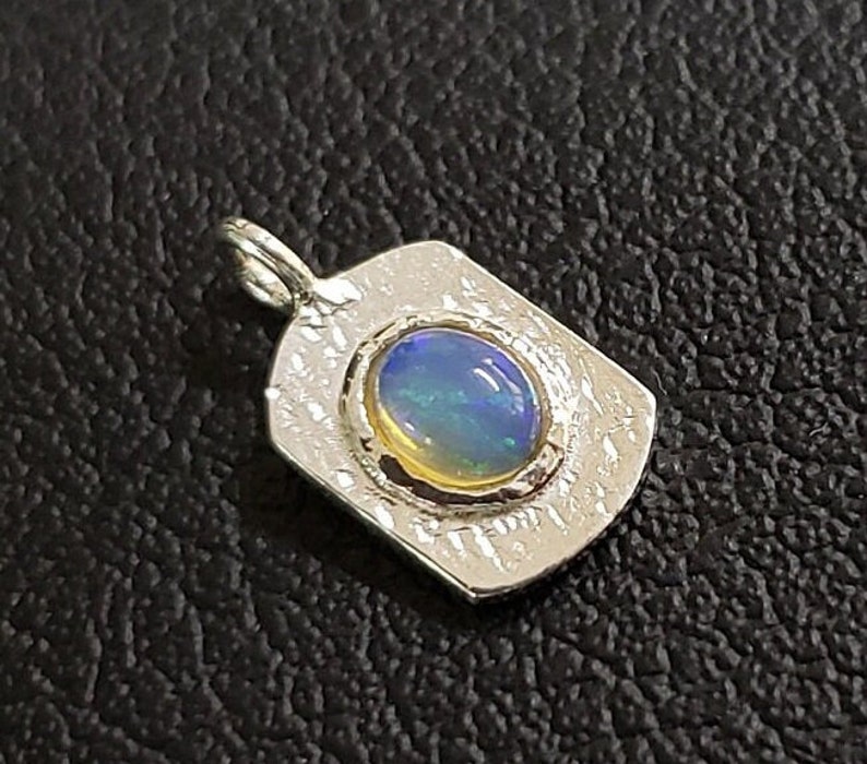 May include: A silver pendant with a textured rectangular design featuring a round opal gemstone with blue and green iridescent colors.