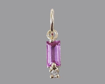 May include: A gold pendant featuring a rectangular, vibrant pink gemstone. Below the pink stone is a small, sparkling diamond accent. The pendant is suspended from a gold loop, perfect for a necklace or bracelet.