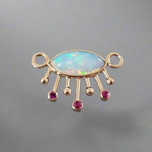 Könnte beinhalten: Goldener Anhänger mit einem weißen Opal-Edelstein in Form eines Auges. Das Auge hat goldene Strahlen, die von ihm ausgehen, mit kleinen Rubin-Edelsteinen an den Enden der Strahlen.