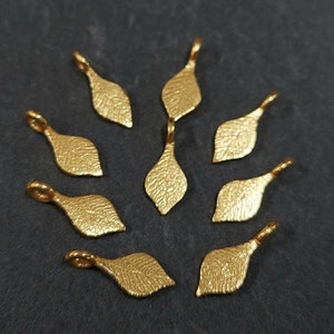 Peut inclure: Dix breloques en forme de feuille dorées avec une surface texturée. Les breloques sont en forme de feuilles et ont une petite boucle en haut pour les attacher à des bijoux ou d'autres objets artisanaux.