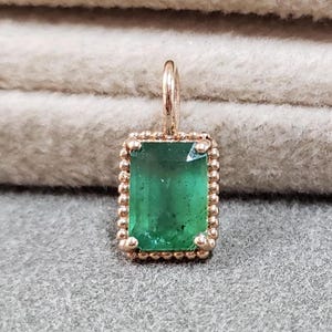 May include: A green emerald gemstone pendant with a gold bezel setting. The pendant is on a white background.