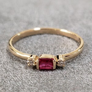 May include: A gold ring with a red gemstone and two smaller clear gemstones.