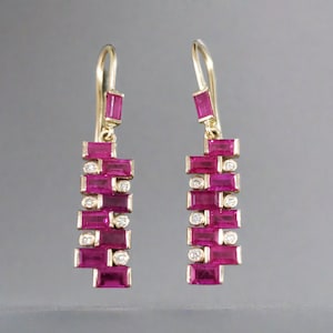 Puede incluir: Un par de pendientes de oro con una cascada de piedras de rubí rosa y diamantes. Los pendientes están diseñados en un patrón geométrico con piedras rectangulares.