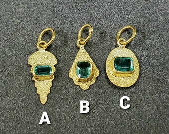 Könnte beinhalten: Drei goldene Anhänger mit grünen Edelstein-Akzenten. Die Anhänger sind in Form einer Träne, eines Blattes und eines Kreises. Die Anhänger sind mit A, B und C gekennzeichnet.