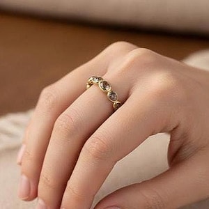 Pu&ograve; includere: Un anello dorato con pi&ugrave; pietre preziose rotonde e trasparenti. L'anello &egrave; su un dito, mostrando il design e la brillantezza del gioiello. La fascia dell'anello &egrave; anch'essa dorata, creando un aspetto coeso ed elegante. Le pietre preziose sono uniformemente distanziate.