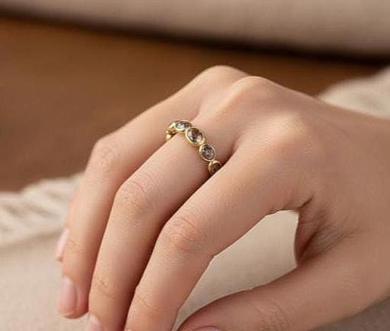 Pu&ograve; includere: Un anello dorato con pi&ugrave; pietre preziose rotonde e trasparenti. L'anello &egrave; su un dito, mostrando il design e la brillantezza del gioiello. La fascia dell'anello &egrave; anch'essa dorata, creando un aspetto coeso ed elegante. Le pietre preziose sono uniformemente distanziate.