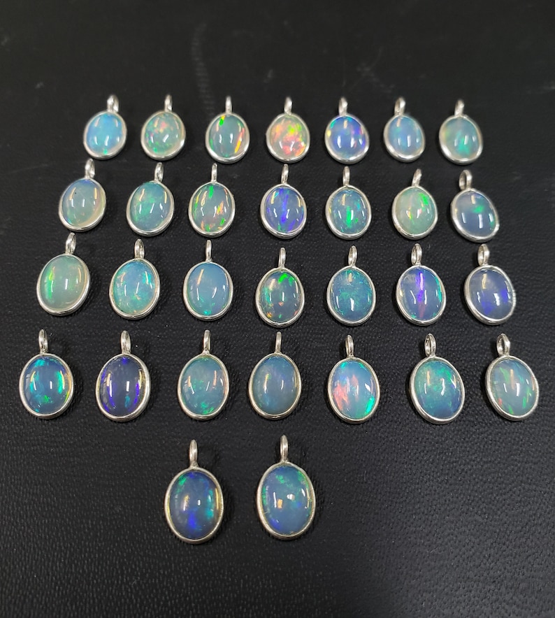 May include: A collection of 25 oval-shaped opal pendants with silver settings. The opals are iridescent with shades of blue, green, and pink.