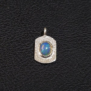 May include: A silver pendant with a textured surface and a blue opal gemstone.