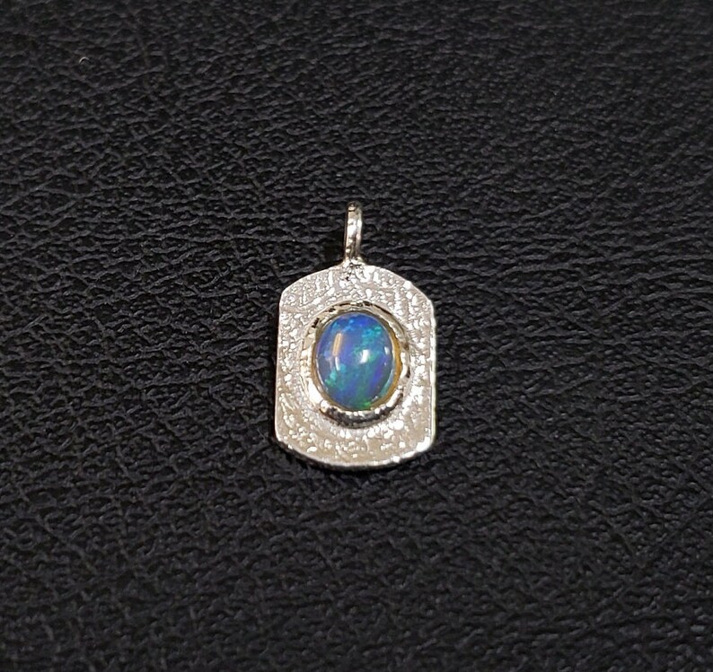 May include: A silver pendant with a textured surface and a blue opal gemstone.
