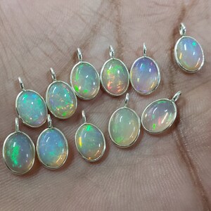 May include: A collection of 12 oval-shaped opal pendants with silver settings. The opals are iridescent with a rainbow of colors.