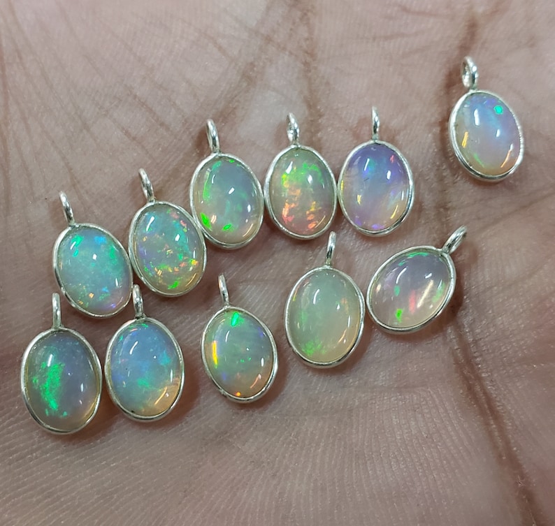 May include: A collection of 12 oval-shaped opal pendants with silver settings. The opals are iridescent with a rainbow of colors.