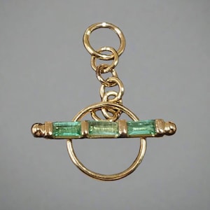 May include: A gold toggle clasp with a chain and a circle. The toggle has four green rectangular gemstones.