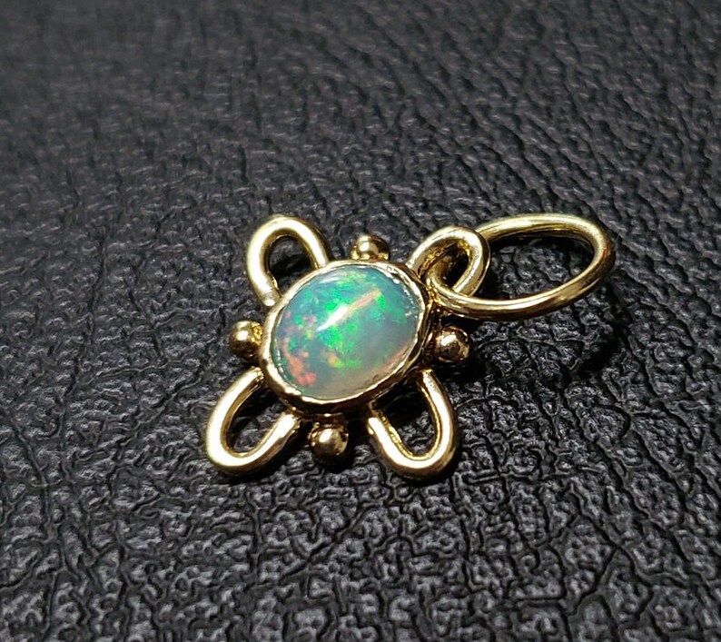 May include: A gold pendant with a delicate, intricate design featuring a round opal gemstone. The opal has a milky white base with flashes of green and blue.