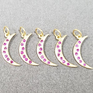 May include: Five gold crescent moon charms with pink gemstones. Each charm has a loop at the top for attaching to a necklace or bracelet.