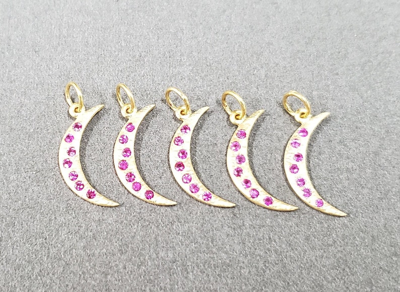 May include: Five gold crescent moon charms with pink gemstones. Each charm has a loop at the top for attaching to a necklace or bracelet.