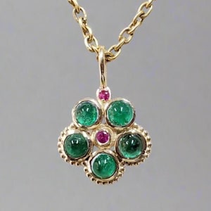 May include: A gold-toned necklace with a pendant featuring five emerald-green gemstones and two smaller ruby-red gemstones. The pendant is flower-shaped, with a delicate chain.