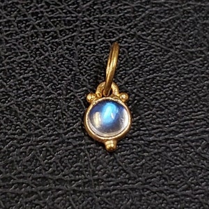 May include: A gold pendant with a blue iridescent gemstone set in a bezel setting. The pendant has a simple design with a loop at the top for attaching to a chain.