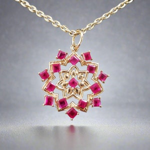 May include: A gold pendant necklace with a delicate, intricate design featuring a central flower motif surrounded by ruby red gemstones.