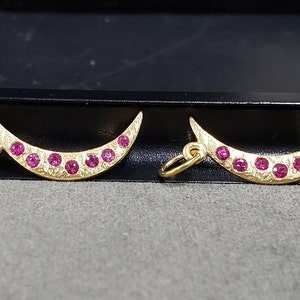 May include: Two gold crescent moon charms with pink gemstones set along the edge.