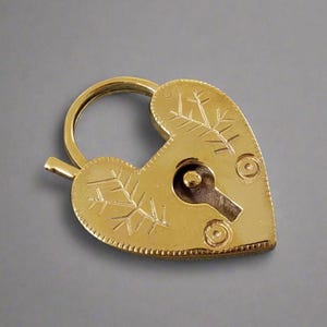 Könnte beinhalten: Ein goldfarbenes herzförmiges Vorhängeschloss mit einem Schlüsselloch und dekorativen, geätzten Designs. Das Vorhängeschloss hat eine Schlaufe zum Anbringen an einer Kette oder einem anderen Objekt.