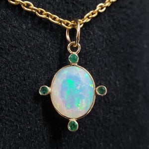 Pode incluir: Um colar de ouro com um pingente que tem uma grande pedra de opala ovalada cercada por quatro pedras verdes menores.