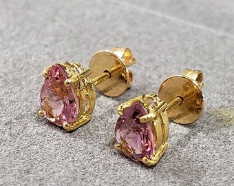 May include: A pair of gold earrings featuring pink pear-shaped gemstones. The earrings have a simple design with a gold setting around the gemstones.
