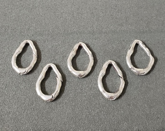 May include: Five silver-colored, teardrop-shaped jewelry clasps. Each clasp has a textured surface and a hinged closure. The clasps are arranged on a gray surface, showcasing their design and potential use in jewelry making.