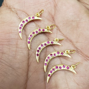 May include: Five gold crescent moon charms with pink gemstones. Each charm has a loop for attaching to a necklace or bracelet.
