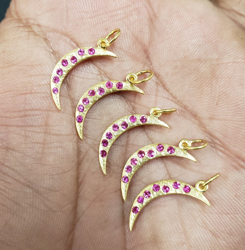 May include: Five gold crescent moon charms with pink gemstones. Each charm has a loop for attaching to a necklace or bracelet.