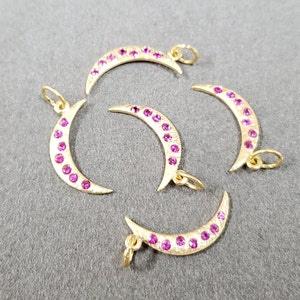 May include: Five gold crescent moon charms with pink gemstones. Each charm has a loop for attaching to a necklace or bracelet.