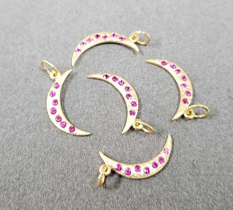 May include: Five gold crescent moon charms with pink gemstones. Each charm has a loop for attaching to a necklace or bracelet.
