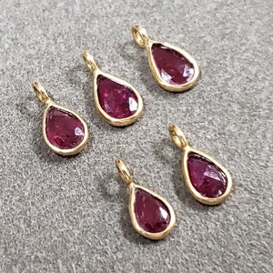 May include: Five gold teardrop-shaped pendants with red gemstone inserts.